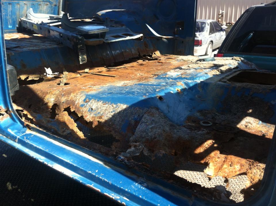 Heavily rusted blue interior of a vehicle with missing floor panels and seats