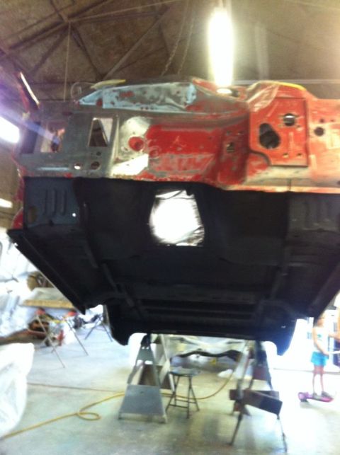 1982 Ford Bronco - The underside of a vehicle is suspended on a lift, revealing its chassis and primer work.