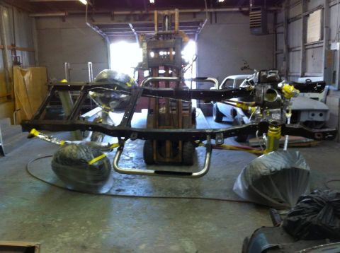 1982 Ford Bronco - A vehicle's chassis is suspended by a forklift, awaiting restoration or assembly.