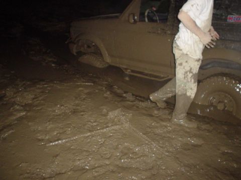 1995 Ford Bronco - A person and their vehicle are deeply stuck in thick mud, with the tires submerged.