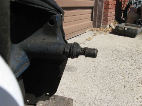 1981 Ford Bronco - Close-up of a greasy automotive component with a metal rod, set against a concrete and garage door background.