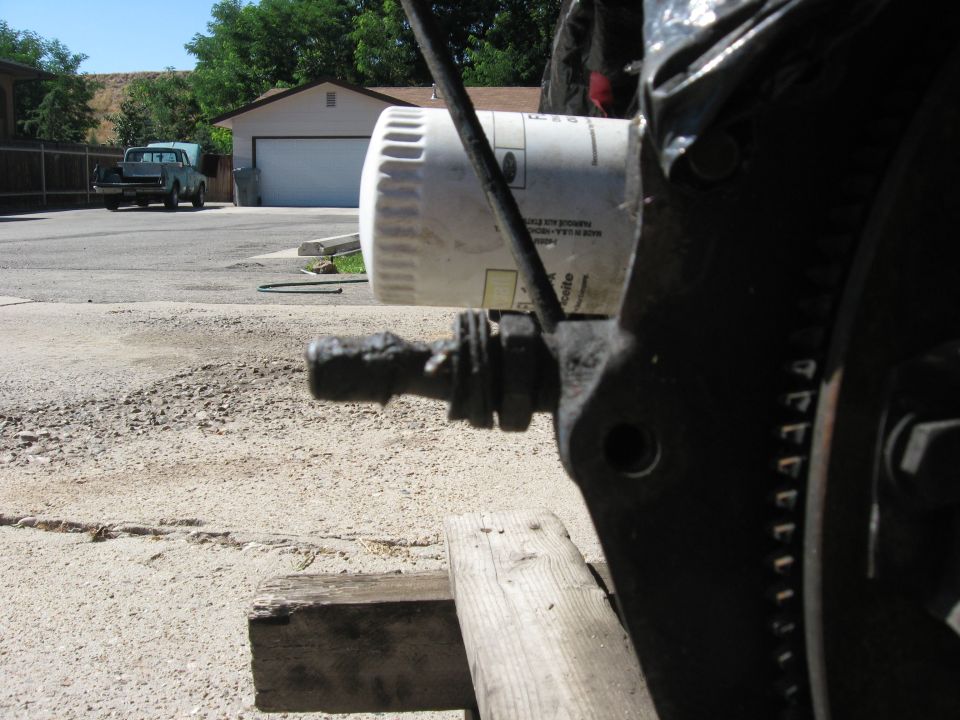 Close-up of engine part and oil filter, with a pickup truck in the background
