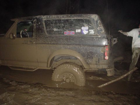 1995 Ford Bronco - A mud-covered SUV is stuck deep in the mud, with a person standing nearby.
