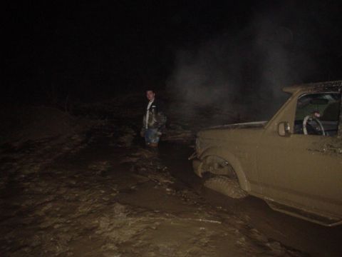 1995 Ford Bronco - A mud-covered 1995 Ford Bronco is stuck in a muddy area at night, with a person standing in the mud nearby.