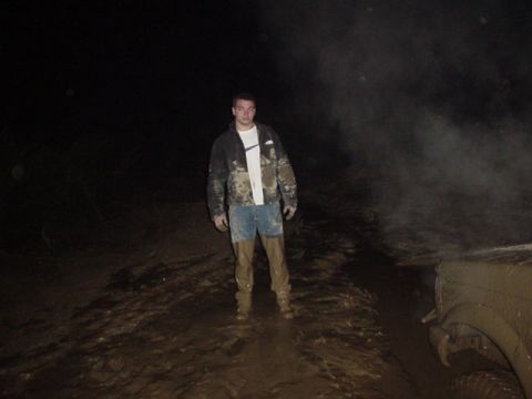 1995 Ford Bronco - Man stands in mud next to a partially visible, mud-covered vehicle at night.