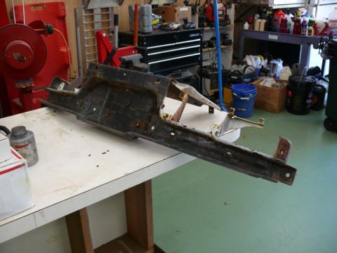 1976 Chevrolet Corvette - A heavily rusted metal frame part sits on a workbench in a garage setting.