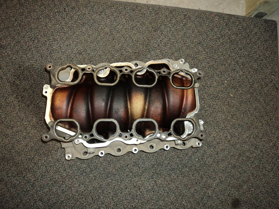 Intake manifold with gasket on textured surface. Supermotors.net logo visible