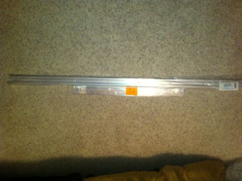 1982 Ford Bronco - Two long aluminum trim or molding strips, one in plastic packaging with a label, lying on a beige carpet.