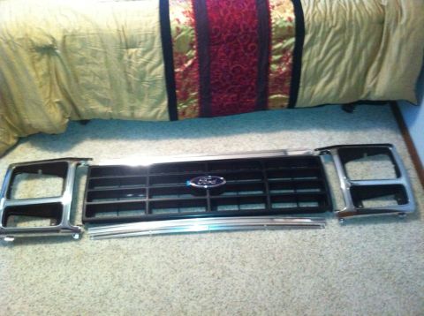 1982 Ford Bronco - Ford grille and headlight surrounds are laid out on a carpeted floor.
