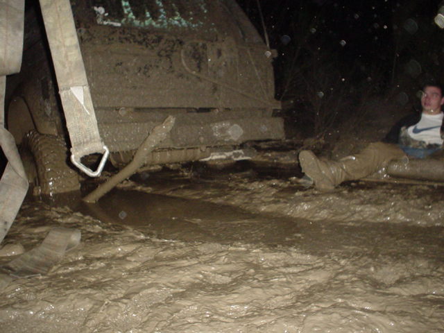 Mud-covered SUV stuck in deep mud at night with a person lying beside it