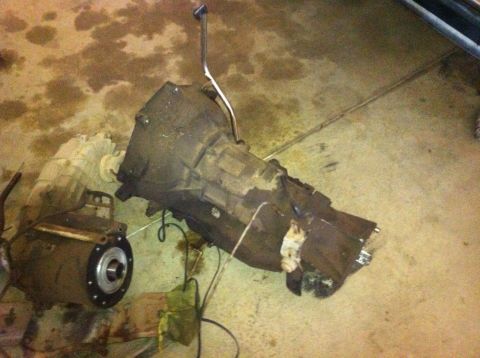 1982 Ford Bronco - Transmission and transfer case components are shown lying on a concrete floor, likely removed from a vehicle for repair or replacement.