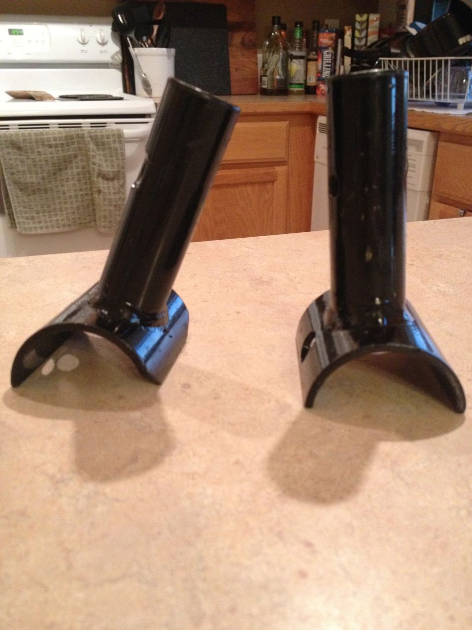 Two black metal brackets with curved bases and cylindrical tops, sitting on a countertop