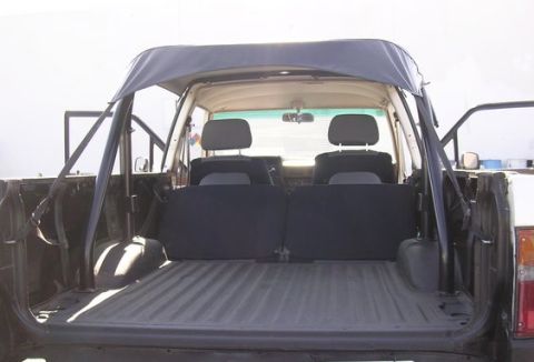 1983 Ferrari Enzo - The interior of a pickup truck is shown from the rear, the bed and rear seating area with a soft top overhead.