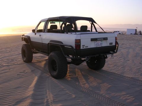 1983 Ferrari Enzo - This modified 1983 Toyota pickup truck with a soft top and large off-road tires is seen on a sandy beach at sunset.
