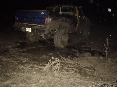 1995 Ford Bronco - This pickup truck is deeply stuck in mud at night, with its rear end facing the camera.