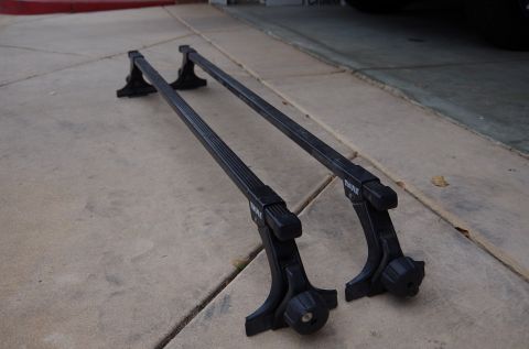 1983 Ferrari Enzo - A pair of black Thule roof rack crossbars and feet are shown resting on a concrete surface.