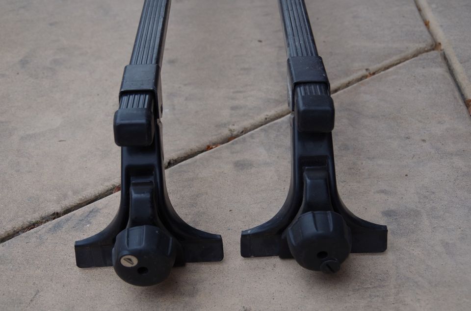Two black roof rack feet with locking mechanisms on a concrete surface