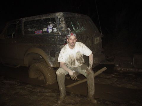 1995 Ford Bronco - A man sits in the mud next to a heavily soiled SUV, possibly a Ford Bronco, stuck in a dark, muddy environment.