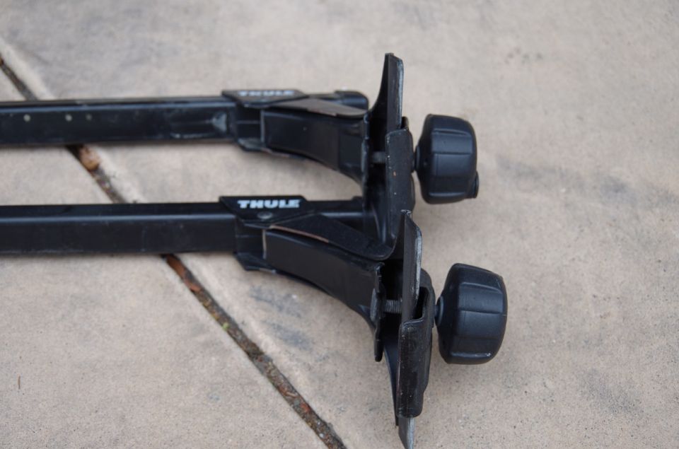 Two black Thule roof rack crossbars with mounting hardware visible
