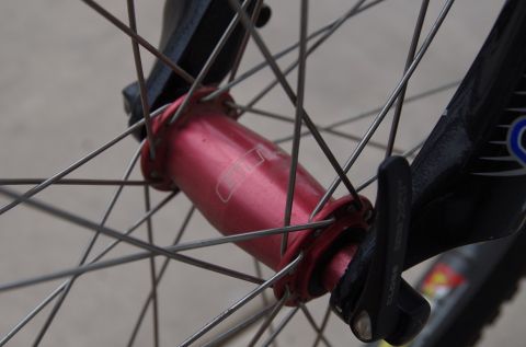 1983 Ferrari Enzo - A close-up shot focuses on the red hub of a bicycle wheel, showing its spokes and a quick-release lever.