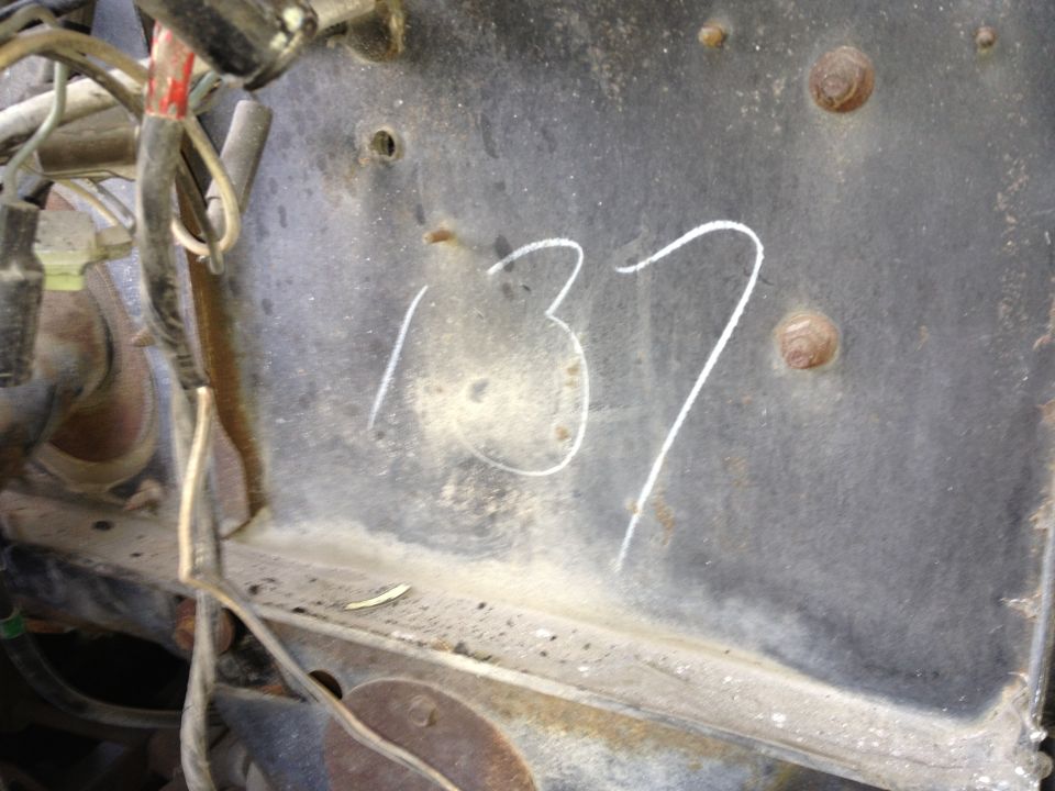 Close-up of a metal surface with '137' written in white chalk, showing bolts and wiring