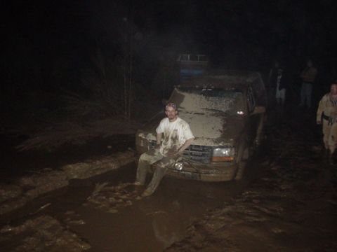 1995 Ford Bronco - A man sits on the hood of a mud-covered truck stuck in a muddy area at night.