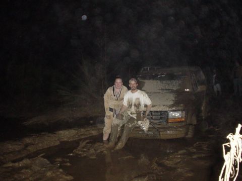 1995 Ford Bronco - Two people stand beside a heavily mud-caked Ford Bronco in a dark, wet environment.