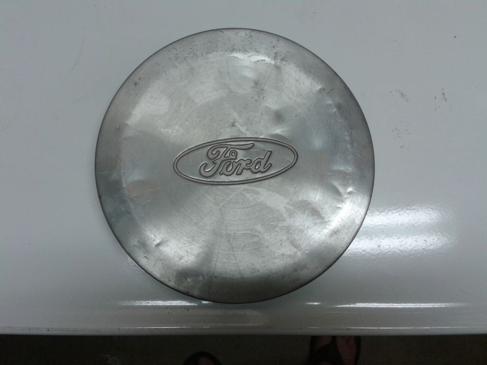 Scratched silver Ford hubcap with dents, showing the Ford oval logo