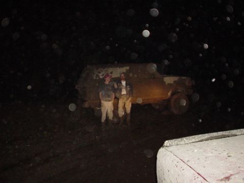 1995 Ford Bronco - Two people stand beside a mud-covered 1995 Ford Bronco, appearing stuck in the dark.