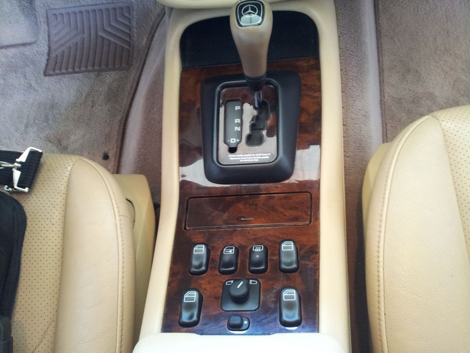Tan leather seats flank a wood-trimmed center console with a gear shifter and multiple window controls in a 2000 Mercedes-Benz ML-Class