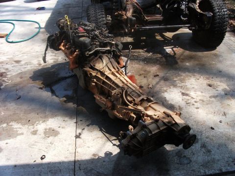 1990 Ford Bronco - Engine and transmission assembly removed from a vehicle, resting on a concrete surface with a partial vehicle frame visible.