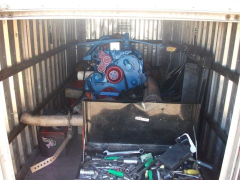 1990 Ford Bronco - A blue engine and a toolbox filled with tools are stored inside a corrugated metal unit.