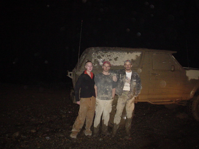 Three muddy people posing at night in front of a mud-covered SUV