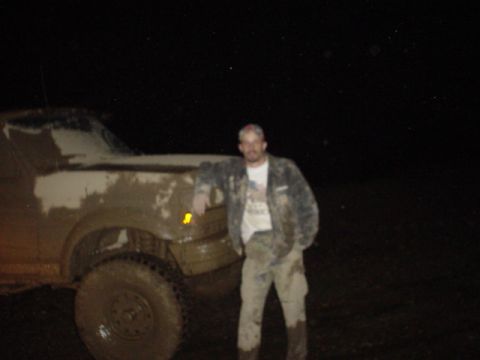 1995 Ford Bronco - A man stands beside a heavily mud-splattered truck at night, its front end visible.