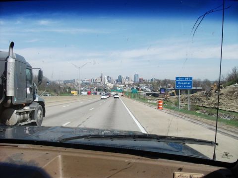 1990 Ford Bronco - View from inside a vehicle on a highway, with a large truck to the left and a city skyline in the distance.