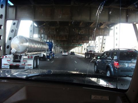 1990 Ford Bronco - View from inside a vehicle driving on a bridge, passing a tanker truck and an SUV.