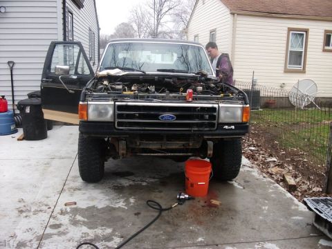 1990 Ford Bronco - 1990 Ford Bronco front view with hood open, parked outside a residential garage.