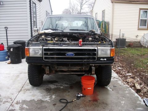 1990 Ford Bronco - A Ford truck sits in a driveway with its hood up, revealing the engine bay and various tools on the ground.
