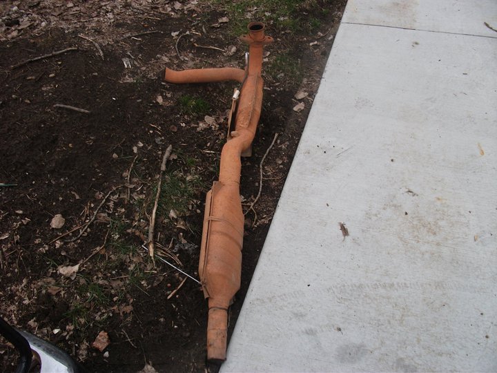 Rusty exhaust pipe and catalytic converter on the ground next to a concrete path