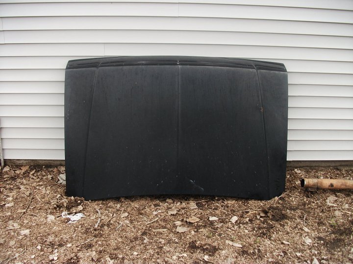 Black hood lying on the ground in front of a white vinyl-sided wall