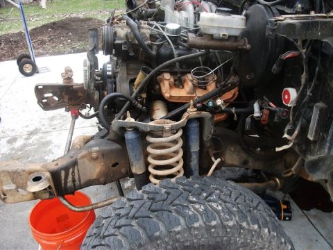 1990 Ford Bronco - Disassembled vehicle engine and chassis components are shown with an orange bucket underneath.