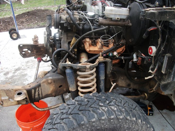 Engine, suspension, and chassis parts of a disassembled vehicle. Orange bucket visible