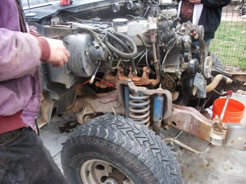 1990 Ford Bronco - The engine bay of a truck is shown, with the front suspension and a tire in view. Text from Supermotors.net is visible.