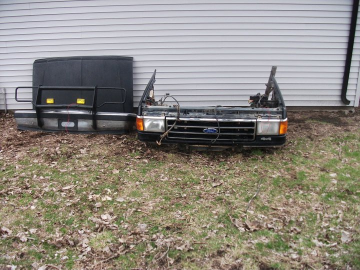 Ford truck front clip with grille and hood leaning against a wall