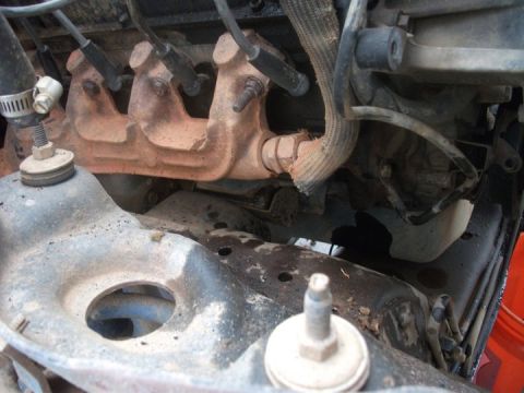 1990 Ford Bronco - Close-up view of an engine's exhaust manifold and associated components, showing spark plug wires and a damaged heat shield.