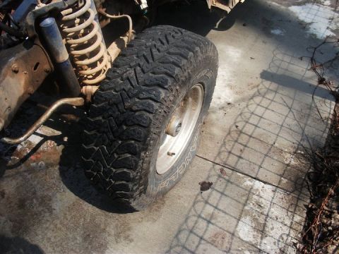 1990 Ford Bronco - Close-up view of a vehicle's front tire and suspension system, with visible off-road tire tread.