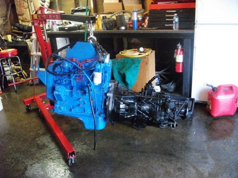 1990 Ford Bronco - A blue engine and black transmission are suspended by an engine hoist in a workshop setting.