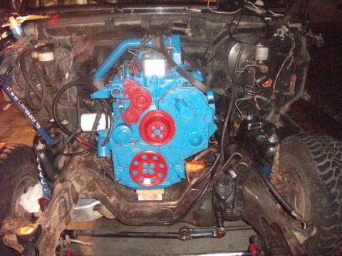1990 Ford Bronco - Engine bay of a vehicle undergoing modification, a bright blue engine with red accents. The Supermotors.net logo is visible in the lower ri…