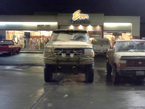 1995 Ford Bronco - A tan Ford Bronco, modified with a brush guard, is parked at a gas station at night, covered in snow.