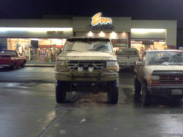 Muddy lifted Ford Bronco parked front-on at night outside an ExtraMile store